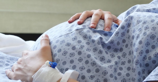 Photo of a pregnant woman in a hospital gown holding her belly.